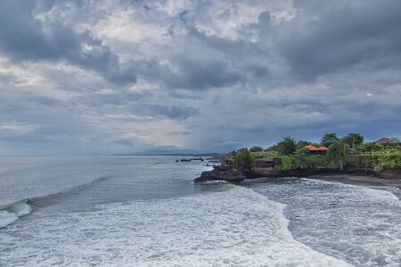 Great nature view of a beach in Tanah Lot Bali with waves hitting it during bad weather with negative space. Motion blur effect due to long exposure techniqueの写真素材