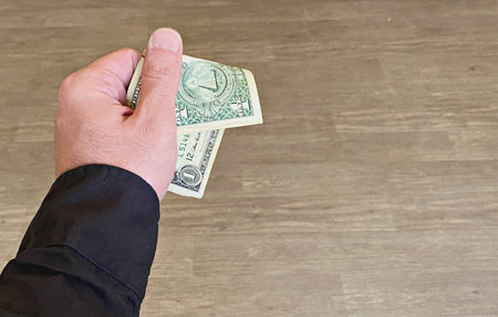 Hand holding one hundred dollar bills on a wooden background.