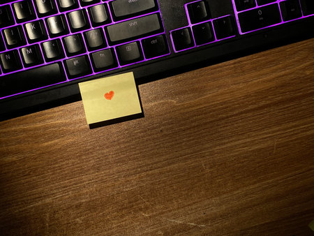 Laptop keyboard and sticky note with heart on it on wooden background