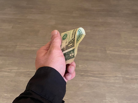 A man's hand holds a dollar bill on a wooden background