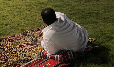 A man in traditional clothes sitting on the grass and reading a book