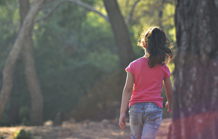 Little girl running in the forest at sunset. Back view. Concept of healthy lifestyle.