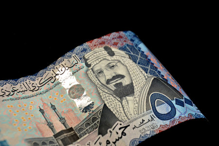 Close-up of a Man's Hand Holding Several Crisp 500 Saudi Riyal Banknotes, Isolated on a White...