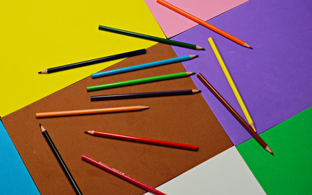 A light blue pen with white wavy lines rests on a stack of colorful foam sheets (yellow, purple,...
