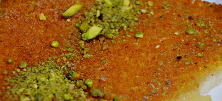 Close up of homemade kataifi pastry with syrup and pistachio nuts on a glass plate with fork. High...