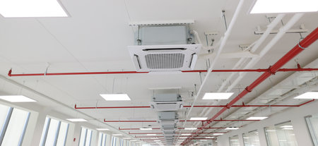 Detailed view of an industrial-style ceiling filled with pipes, lights, and electrical wiring. The infrastructure supports museum or exhibit lighting and air systems.の写真素材