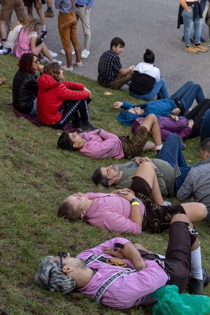 Munich, Germany, 2019 September 19: 4 mans sleeping in a row on the lawn at the Bavarian Oktoberfest in Munichのeditorial素材