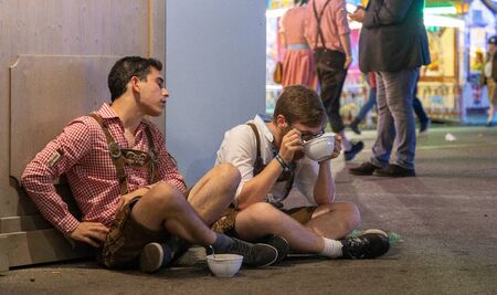 Munich, Germany - September 24: 2 drunk male visitors sitting on the ground and eating a soup at the oktoberfest.のeditorial素材