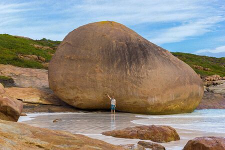 young caucasian man in front of a huge rock at Lucky Bay, Cape Le Grand National Park near Esperanceの写真素材