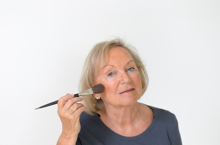 Attractive middleaged woman applying makeup with a large soft cosmetics brush to smooth out the signs of wrinkles and agingの写真素材