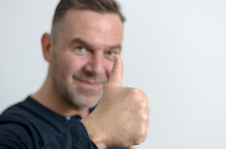 Blue eyed middleaged man with a positive attitude smiling while showing thumb up portrait with copyspace on grayの写真素材