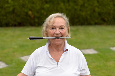 Head and Shoulders Portrait of Mature Woman Acting Playful Grasping Knife Sharpener Between Teethの写真素材