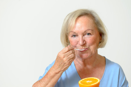 Happy friendly smiling senior lady with a fresh healthy orange in her hand in a healthy diet and nutrition conceptの写真素材