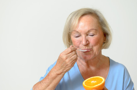 Happy friendly smiling senior lady with a fresh healthy orange in her hand in a healthy diet and nutrition conceptの写真素材