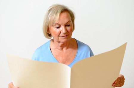 Elderly lady holding a blank paper sheet big holes and looking at it as at an empty newspaper portraitの写真素材