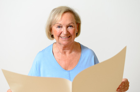 Elderly lady holding a blank paper sheet big holes and looking at it as at an empty newspaper portraitの写真素材