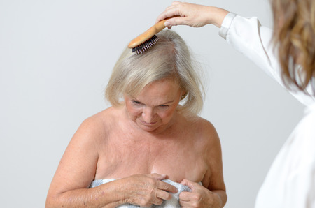 Elderly lady gets her hair combed maybe she lives in a home for old people and care needsの写真素材
