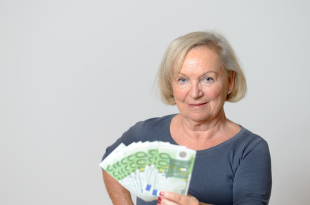 Close up Adult Blonde Woman Holding Fan of Hundred Euro Banknotes Isolated on Light Gray Wall.の写真素材
