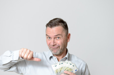 Close up Adult Man Holding a Fan of Five Euro Notes While Looking at the Camera Against Light Gray Wallの写真素材