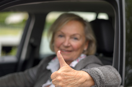 Elderly woman sitting in a car with thumb up while looking to the cameraの写真素材