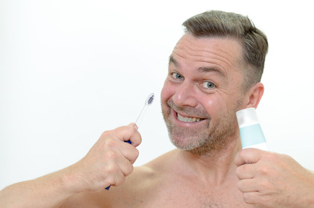 Charismatic man looking at the camera with a comic expression with a toothbrush and toothpaste in his handの写真素材