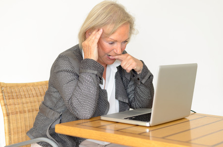 Active blond senior woman with formal clothes sitting thoughtful at a  desk in front of a silver laptopの写真素材