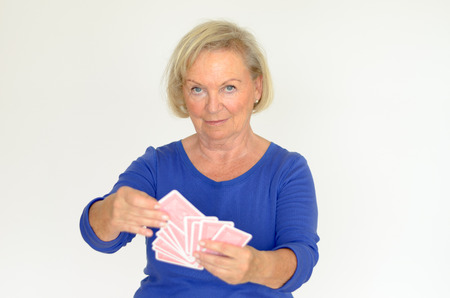 Smiling woman holding a fanned hand of playing cards Selecting one from the pack with a smile upper body over grayの写真素材