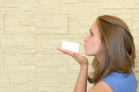 Close up Pretty Blond Young Woman Kissing a Small White Card with Copy Space on her Hand.の写真素材