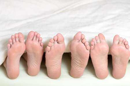 Three pairs of feet in bed, all looking upwards