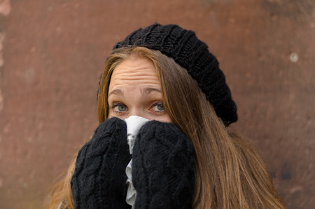 Close up Sick Young Woman in Winter Attire Blowing her  Using Handkerchief While Looking at the Camera.の写真素材