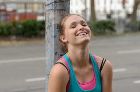 Close up Thoughtful Sporty Young Woman Leaning Against the Post at the Street with a Happy Face and Eyes are Closed.の写真素材