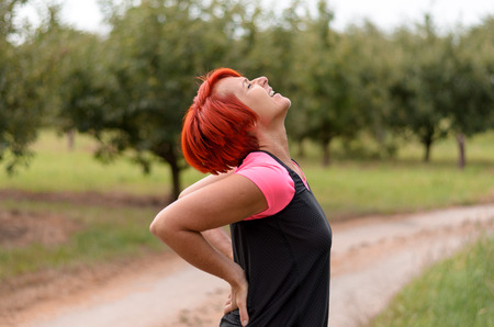 Half body Shot of an Adult Redhead Woman Holding her Painful Lower Back While Doing an Outdoor...