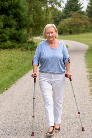 Full Length Shot of a Middle Aged Woman Walking on the Pathway with Two Canes and Smiling at the Camera.の写真素材