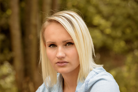 Pretty blond woman with a trendy haircut looking at the camera with a serious expression, head and...