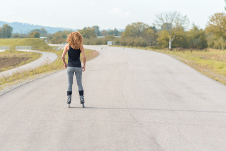 Muscular sporty young woman on roller blades standing facing away from the camera on a rural road in an exercise and healthy active lifestyle conceptの写真素材