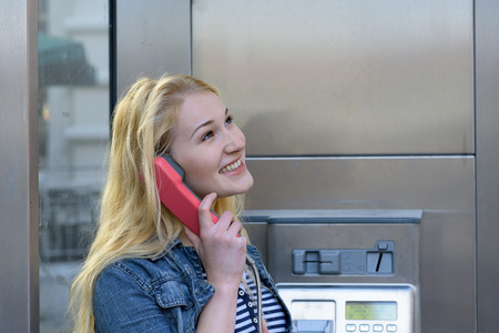 smiling young blond woman on the phone in a phone booth while looking upの写真素材