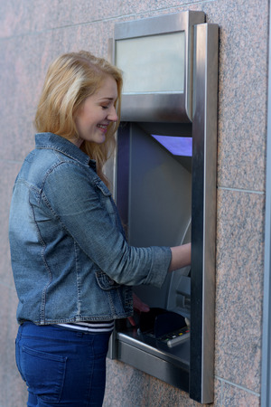 Stylish woman drawing money at an outdoor bank ATM holding a handful of banknotes and turning to give the camera a lovely smileの写真素材