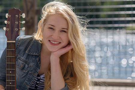 young blonde woman with a guitar on a lake while looking at the cameraの写真素材