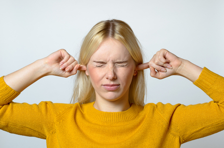 Close up Disgusted Young Woman Covering her Ears with Fingers, with Eyes Closed, Against Gray Background.の写真素材