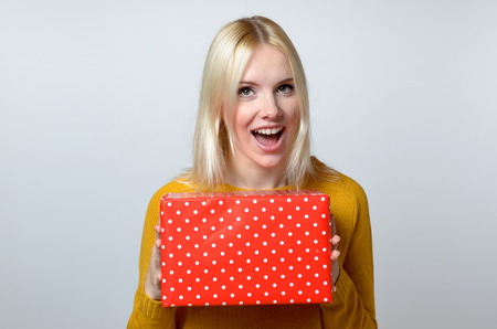 Happy Blond Young Woman Holding Red Gift Box Against White Background.の写真素材