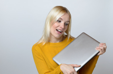 Very Happy Young Woman Holding a Brand New Laptop Computer with Mouth Open Against White Backgroundの写真素材