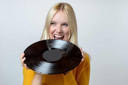 Half Body Shot of a Young Woman biting a Vinyl Record, Against White Background.の写真素材