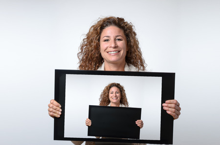 Friendly smiling attractive young woman holding up a computer or television monitor in her hands...