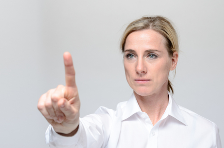 Businesswoman pressing a virtual button against grey backgroundの写真素材