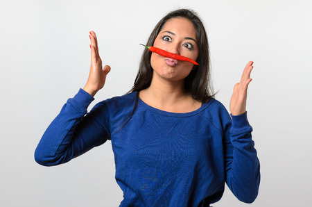 Goofy woman with a red hot chili pepper mustache balanced on her lip squinting and gesturing with her hands, upper body over whiteの写真素材