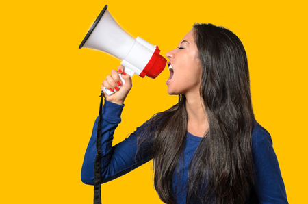 Young woman shouting into a megaphone, side view on orange conceptual of a rally or protestの写真素材