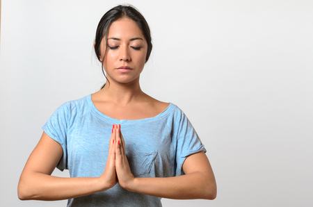 Young woman practicing yoga having her hands in front with a serene serious expression, upper body on white in a wellness and healthy lifestyle conceptの写真素材
