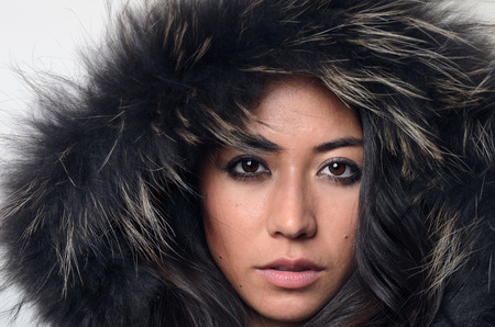 Pretty young woman in a furry hood looking directly at the camera with a serious expression conceptual of winter fashion and beautyの写真素材