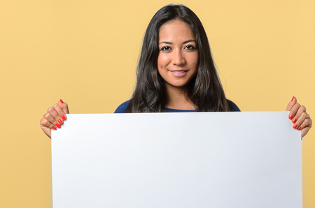Smiling attractive young woman holding a blank white sign with copy space for your text that she is holding in front of her chestの写真素材