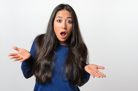 Young woman shrugging her shoulders and gesturing with her hand with her mouth open in protest as she shows her ignorance or innocenceの写真素材